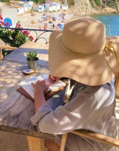 “Anne-Lies Smal schrijvend in de zon, met een hoed op een Spaans terras – een liefsbrief over volle bloei