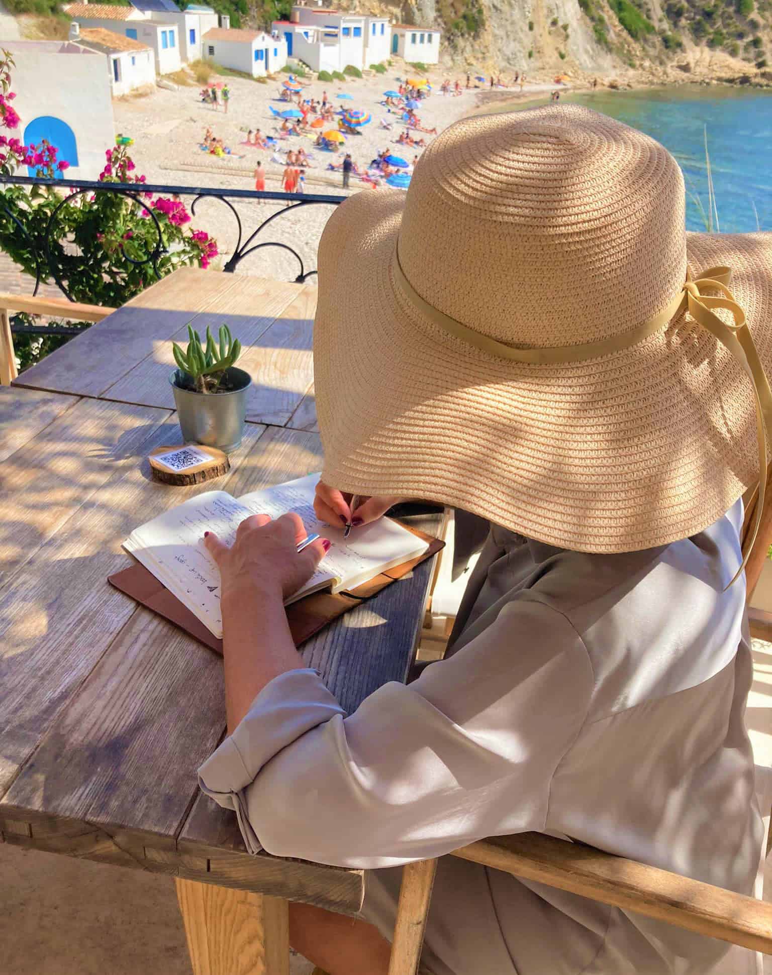 “Anne-Lies Smal schrijvend in de zon, met een hoed op een Spaans terras – een liefsbrief over volle bloei